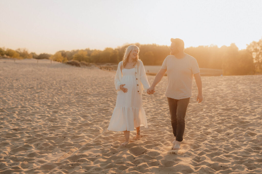babybauchshooting boberger duenen, schwangere und partner hand in hand im sonnenuntergang