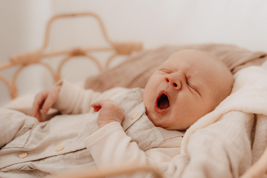newbornshooting, baby liegt im korb und gaehnt