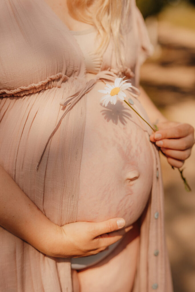 babybauchshooting boberger duenen, schwangere haelt blume in der hand und der schatten faellt auf babybauch