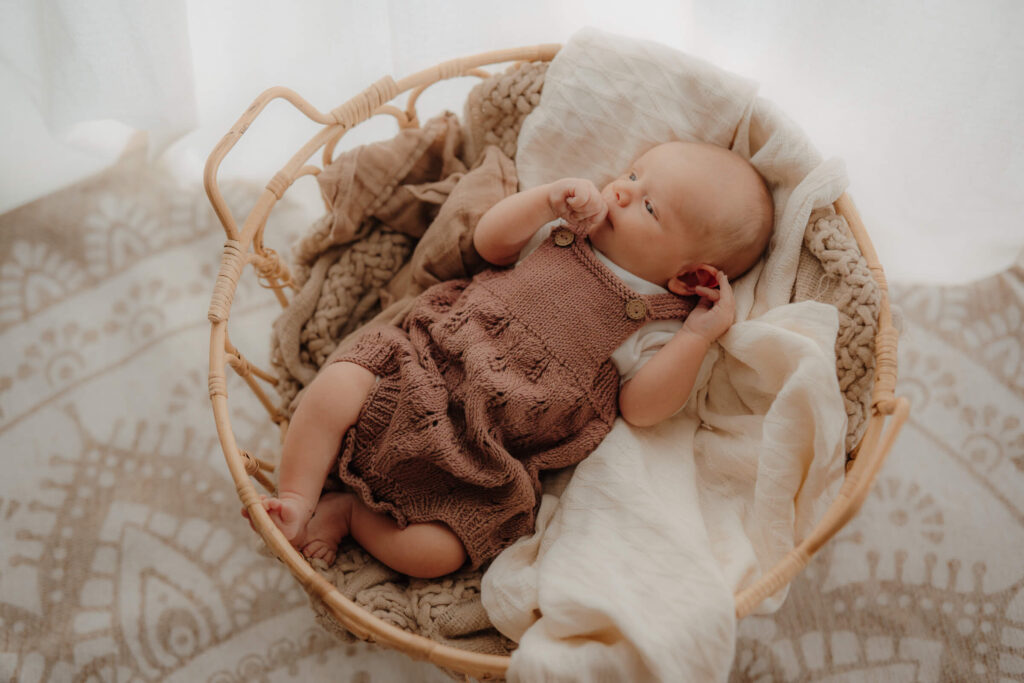 newbornshooting, baby liegt im korb und guckt zufrieden